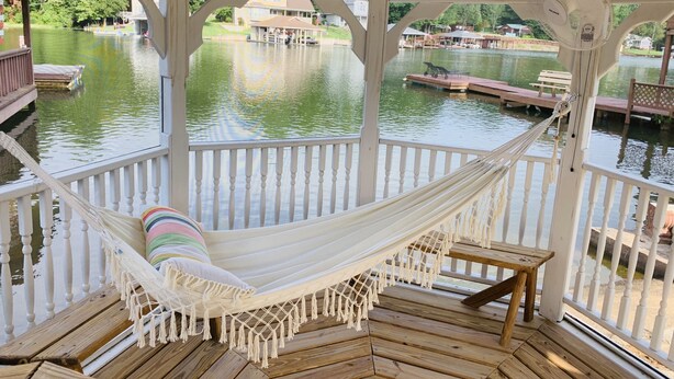 Una hamaca en una terraza de madera con vista a un lago y barcos.