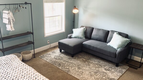 A room with a grey sectional sofa, a patterned rug, a hanging rack with clothes, and a floor lamp. - Incredible Lake Harding Waterfront home!! (Salem)