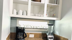 Una cocina con cafetera, licuadora y copas de vino sobre la encimera.