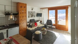 Una sala de estar moderna con un sofá, una televisión y vistas a un paisaje nevado a través de amplios ventanales.