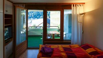 A bedroom with a bed, a television, and a sliding glass door leading to a balcony with a table and chairs.