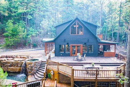 A cabin with a deck, a hot tub, and a stone waterfall feature.