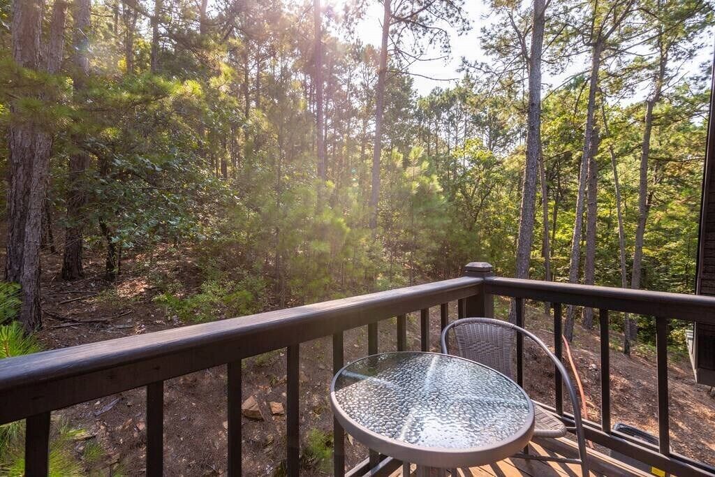 Una terraza con mesa de vidrio y silla de metal, rodeada de un bosque.
