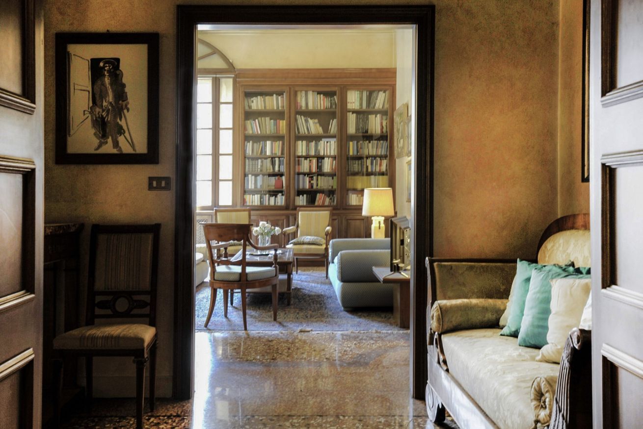 A room with a wooden chair, a sofa, a small table, and a bookshelf filled with books.