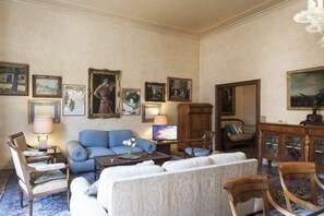 A traditional living room with a blue sofa, a wooden cabinet, and various framed artworks on the walls.