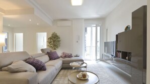 Ein modernes Wohnzimmer mit einem beigen Sofa, einem Couchtisch mit Dekoration, einem Fernseher und einem Bücherregal.