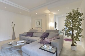 Een moderne woonkamer met een grijze bank, een bijzettafeltje en een potplant.