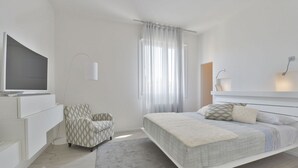 Ein modernes Schlafzimmer mit Bett, Fernseher, Sessel und Schreibtisch.