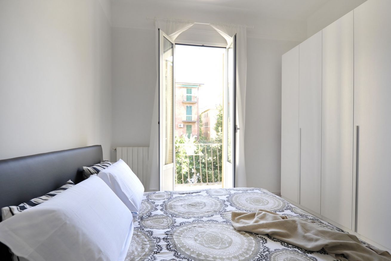 A bedroom with a bed, a window, and a view of buildings outside.