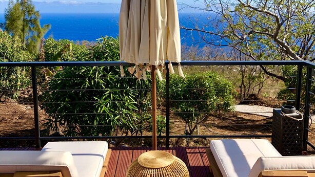 A wooden deck with lounge chairs and a woven basket, overlooking a scenic view of the ocean and mountains. - Charming chalet with large terrace and breathtaking sea view (Saint-Leu)