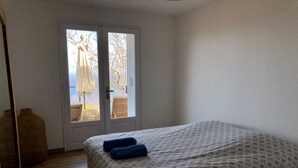 A bedroom with a bed, a door leading to an outdoor area, and a wicker chair. - Charming chalet with large terrace and breathtaking sea view (Saint-Leu)