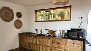 A kitchen with a wooden cabinet, a microwave, a sink, and a window with a view of greenery. - Charming chalet with large terrace and breathtaking sea view (Saint-Leu)
