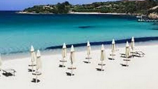 Ein Strand mit weißen Sonnenschirmen und blauem Meer.