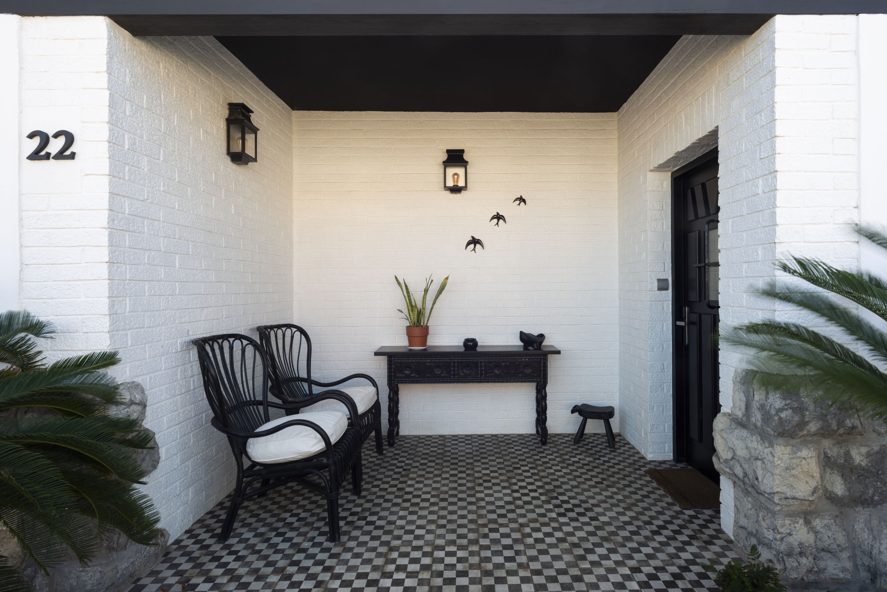 A checkered floor, a black bench, two chairs, a table with a potted plant, and a door with a number 22 sign.
