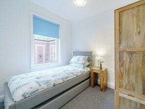 Ein kleines Schlafzimmer mit einem Einzelbett, einem Fenster, einem Nachttisch und einem Holzschrank.