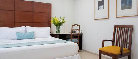 Habitación de hotel con una cama grande, cabecero de madera, escritorio con silla y dos cuadros en la pared.