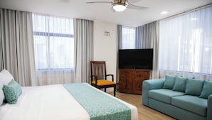 Una habitación de hotel con cama, sofá, televisor y cortinas.
