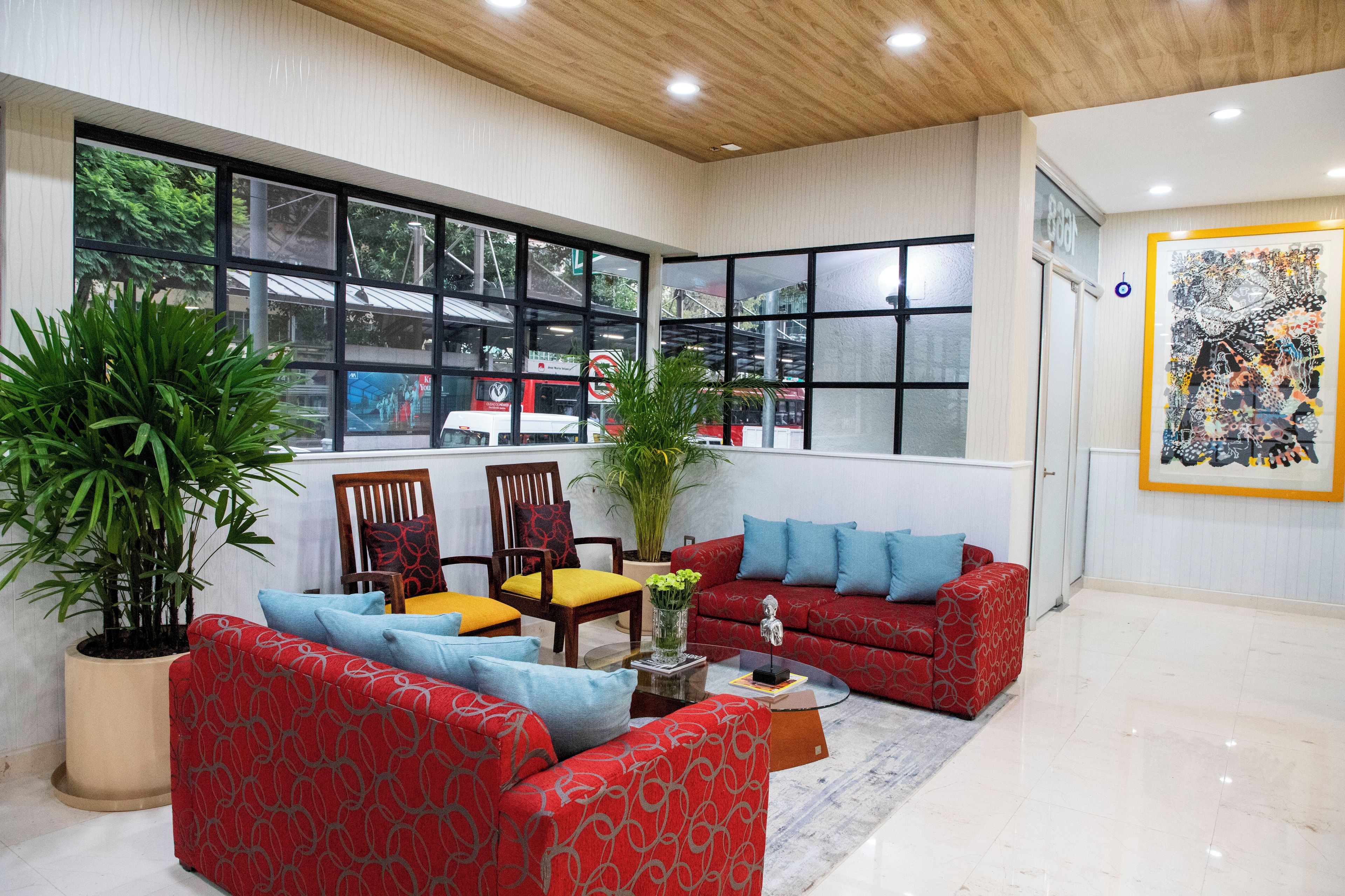 A spacious living room with a red sofa, blue cushions, a wooden coffee table, and large windows offering a view of the outside.