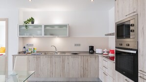 A modern kitchen with a glass-top dining table, stainless steel appliances, and light wood cabinetry. - Casa Mercedes, Apt 1 - Sea View and Terrace, Puerto del Carmen - Lanzarote (Puerto del Carmen)