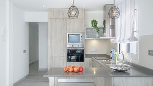 Cocina moderna con una isla central, dos taburetes negros, microondas, horno y una planta colgante.