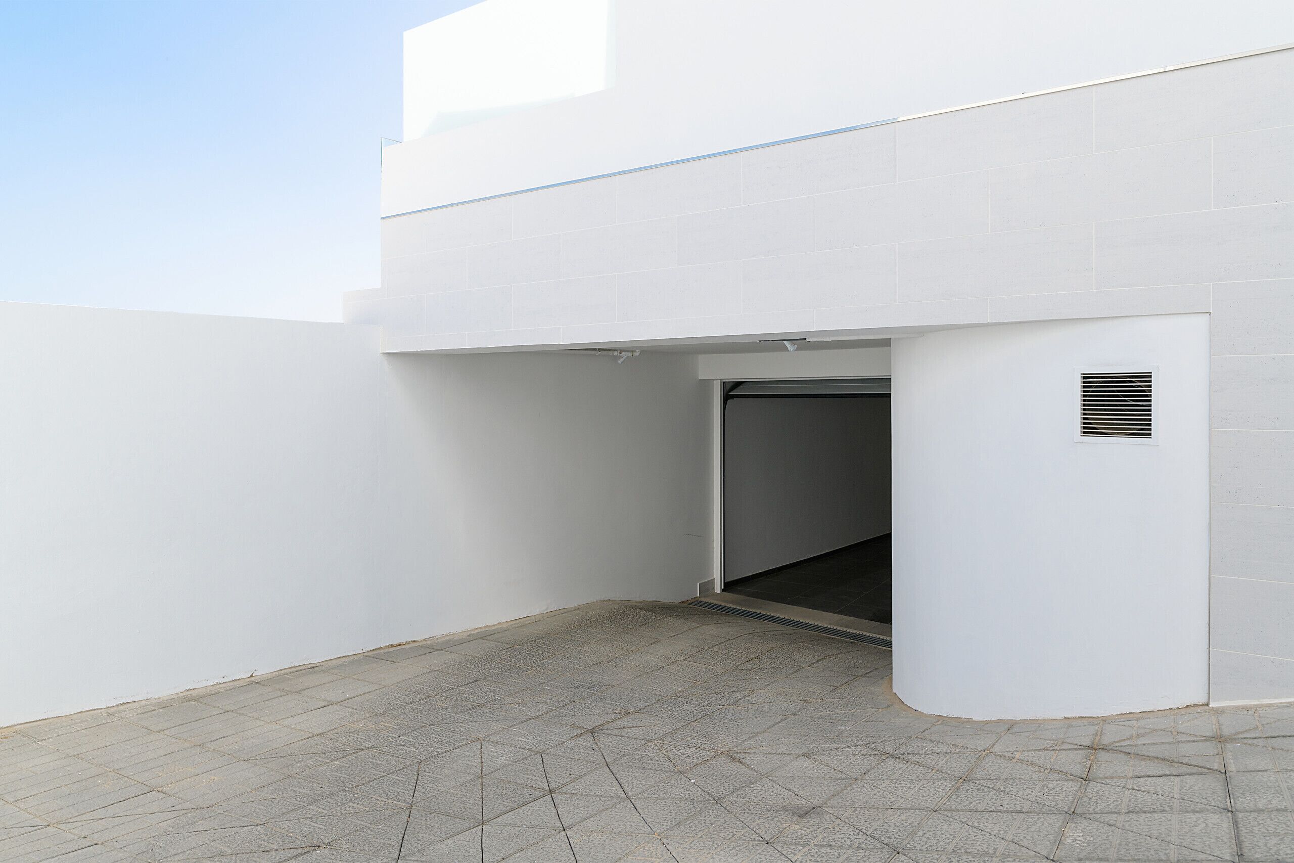 A clean, modern building exterior with a white facade, a visible door, and a tiled floor.