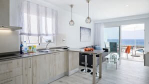 Cocina moderna con una isla grande, comedor con mesa de vidrio y vista al mar a través de amplios ventanales.