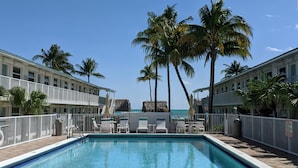 A pool area with lounge chairs and palm trees, surrounded by buildings with balconies. - Beachside Unit 09 - Key Colony (Key Colony Beach)