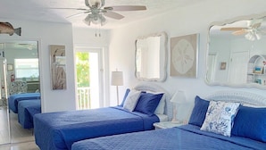 A room with three beds, each with blue bedding, a ceiling fan, and a view of the outdoors. - Beachside Unit 09 - Key Colony (Key Colony Beach)