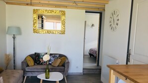 Een gezellige woonkamer met een bank, een klein rond tafeltje, een spiegel en een klok aan de muur.