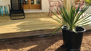 Een houten terras met een zwarte stoel, een rode metalen stoel en een bloempot.