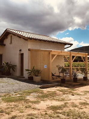 Un bâtiment doté d’un toit en tuiles, d’une pergola en bois et de plantes en pot.