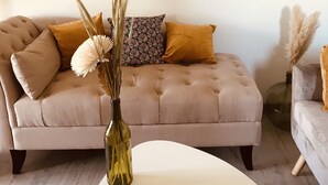Een woonkamer met een beige bank, een rond bijzettafeltje en een vaas met gedroogde planten.