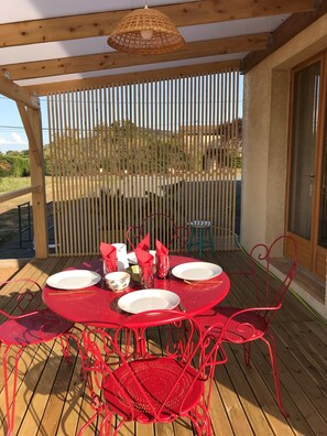 Un espace extérieur abrité, aménagé pour les repas, avec une terrasse en bois, du mobilier en métal rouge et un luminaire suspendu au plafond, fait de bambou.