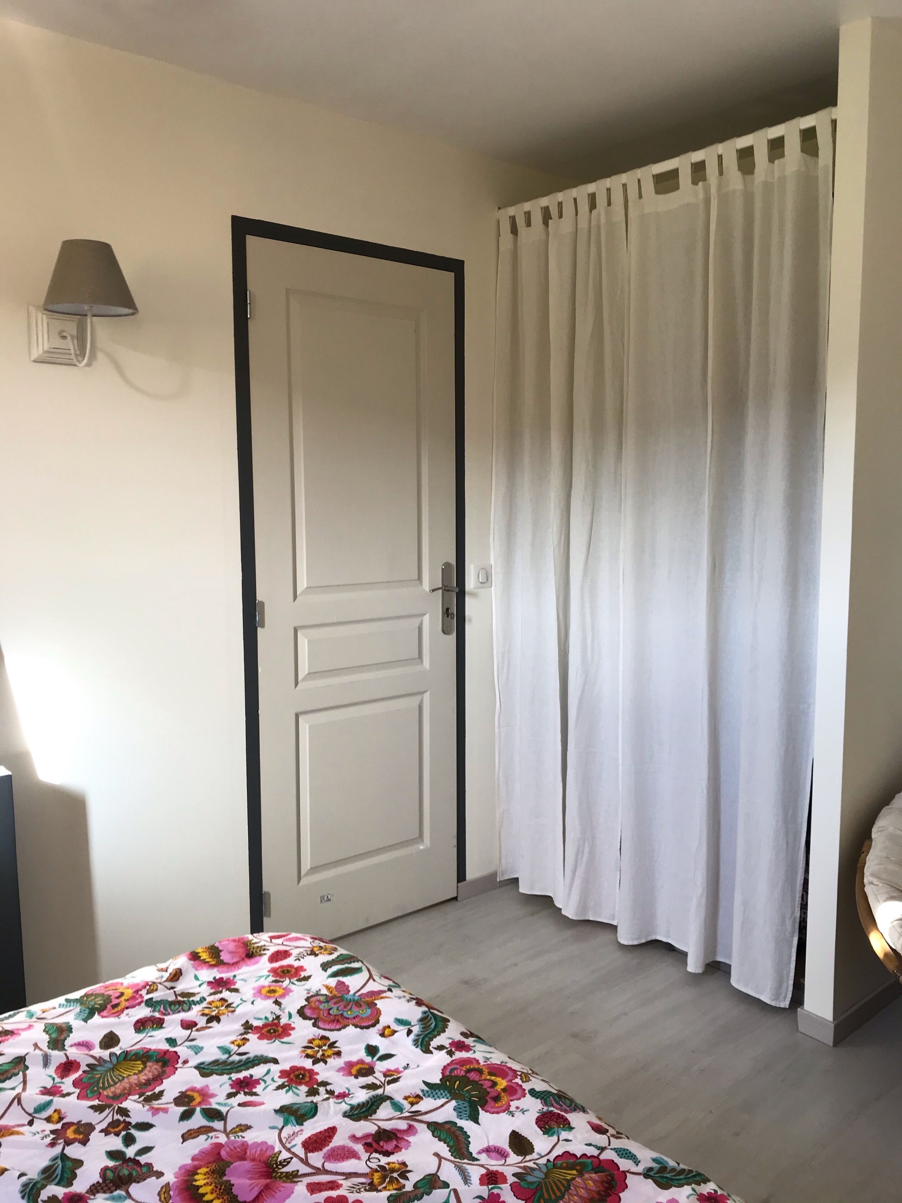 A room with a bed, a door, a curtain, and a wall-mounted lamp.