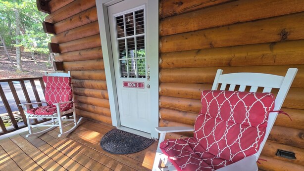 A wooden cabin with a porch, two rocking chairs with red cushions, a white door with a window, and a doormat. - Standard Guest Room (Main) - Barefoot Hills - North Georgia Mountains (Dahlonega)
