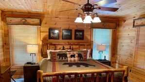 Une chambre dans une cabane en bois, avec un lit, une table de chevet, une commode et un ventilateur de plafond.