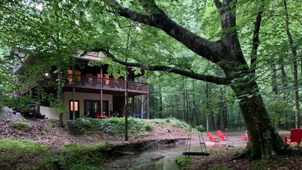 Une cabane dotée d’un balcon donnant sur une zone boisée et un ruisseau.