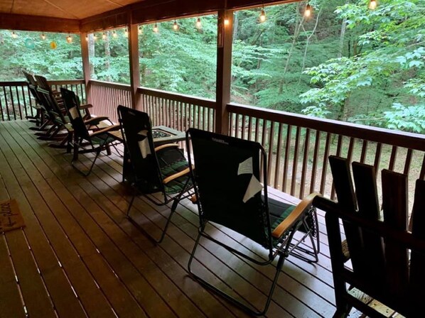 A wooden deck with rocking chairs and a view of a forest.