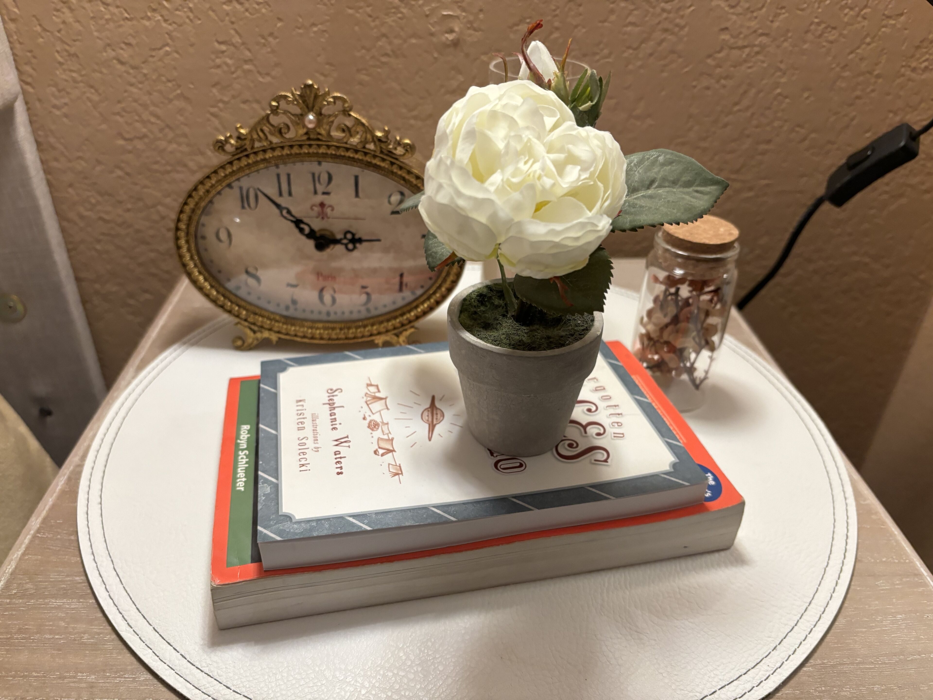 A white table with a clock, a potted plant, and a book.