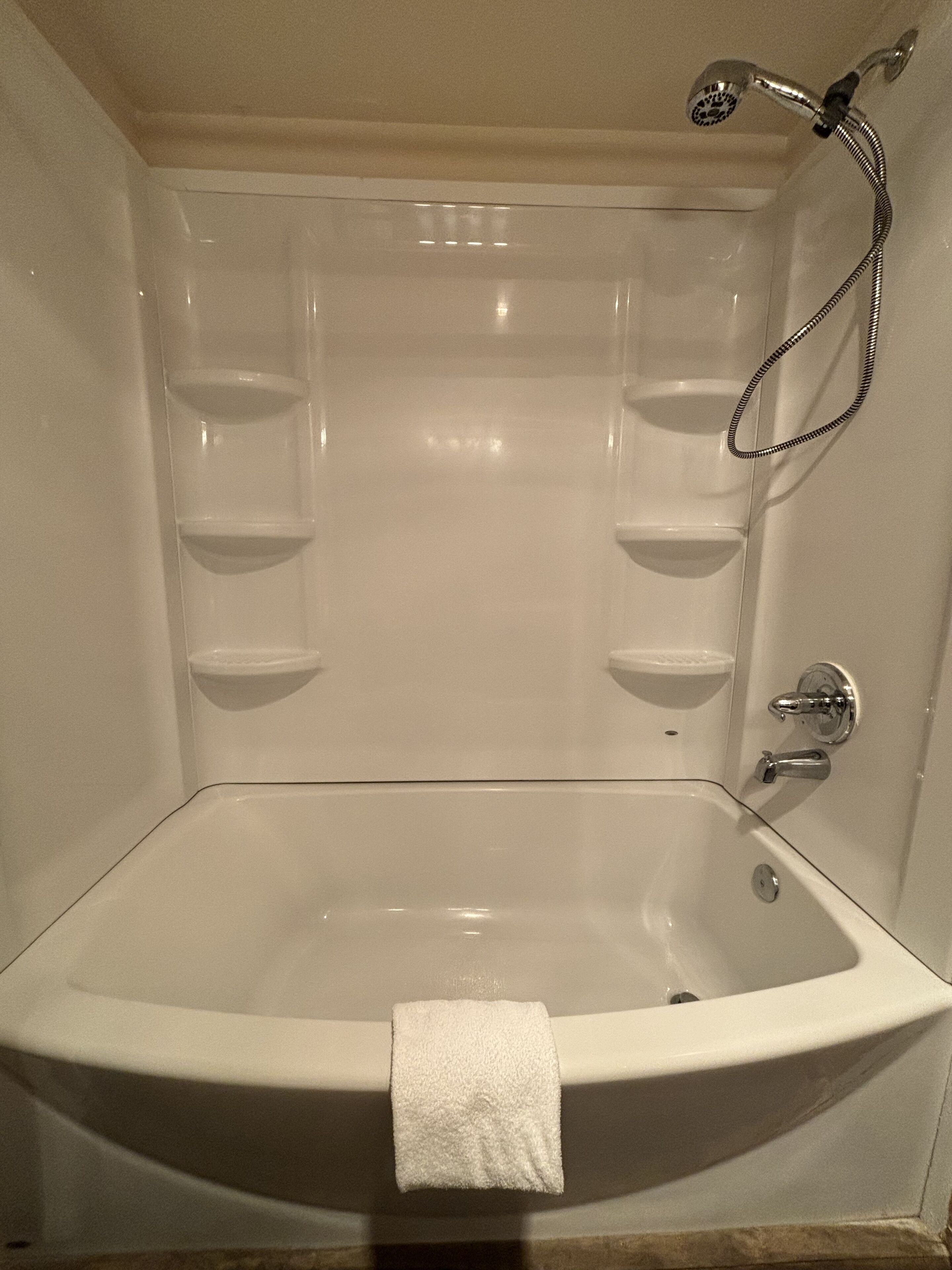 Een groot, leeg bad met douchekop en bedieningsknoppen, en een handdoek aan de zijkant.