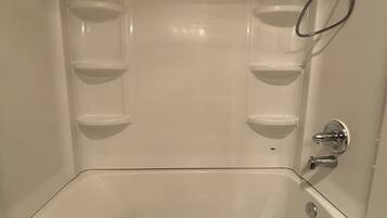 A large, empty bathtub with a shower head and control knobs, and a towel hanging on the side.