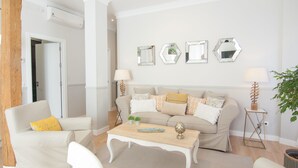 A living room with a beige sofa, white armchairs, a wooden coffee table, and a wall with hexagonal mirrors. - Stylish Apt PZA MAYOR / La Latina 2BD * 2BT *, 6p max (Madrid)
