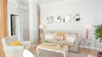 Una sala de estar con un sofá beige, sillones blancos, una mesa de centro de madera y una pared con espejos hexagonales.