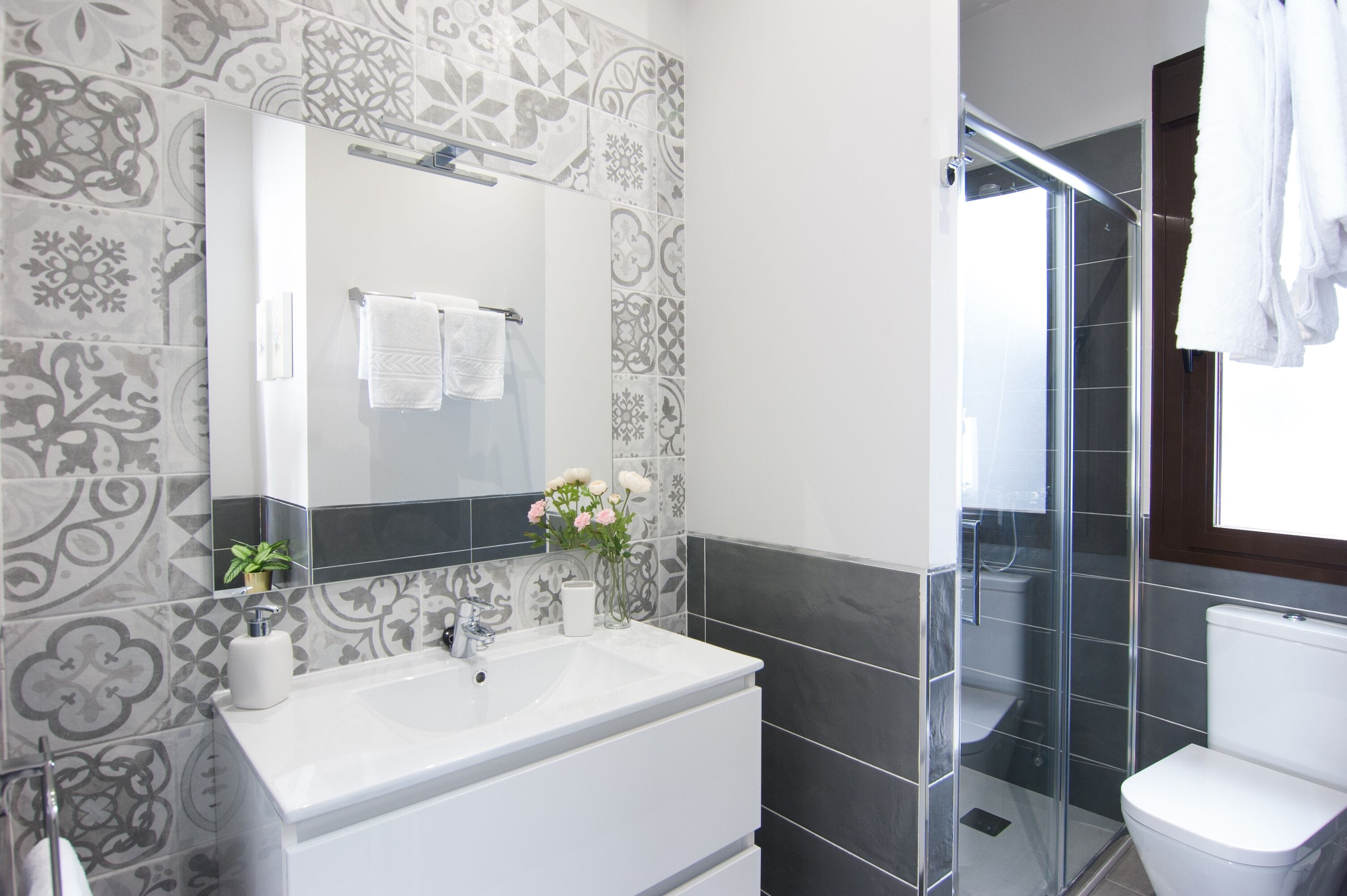 Un baño moderno con un espejo grande, lavabo blanco y cabina de ducha de vidrio.