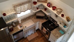Une cuisine compacte équipée d’un évier, d’une cuisinière, d’un four à micro-ondes et d’une petite fenêtre agrémentée d’un rideau à carreaux.