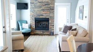 Un salon avec une cheminée en pierre, un fauteuil bleu, un canapé beige et une table basse en bois.