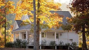 Une maison blanche dotée d’un porche, entourée d’arbres aux feuilles d’automne.