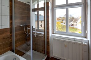 Un baño moderno con cabina de ducha de vidrio, una bañera blanca y una ventana con vistas a una zona residencial.