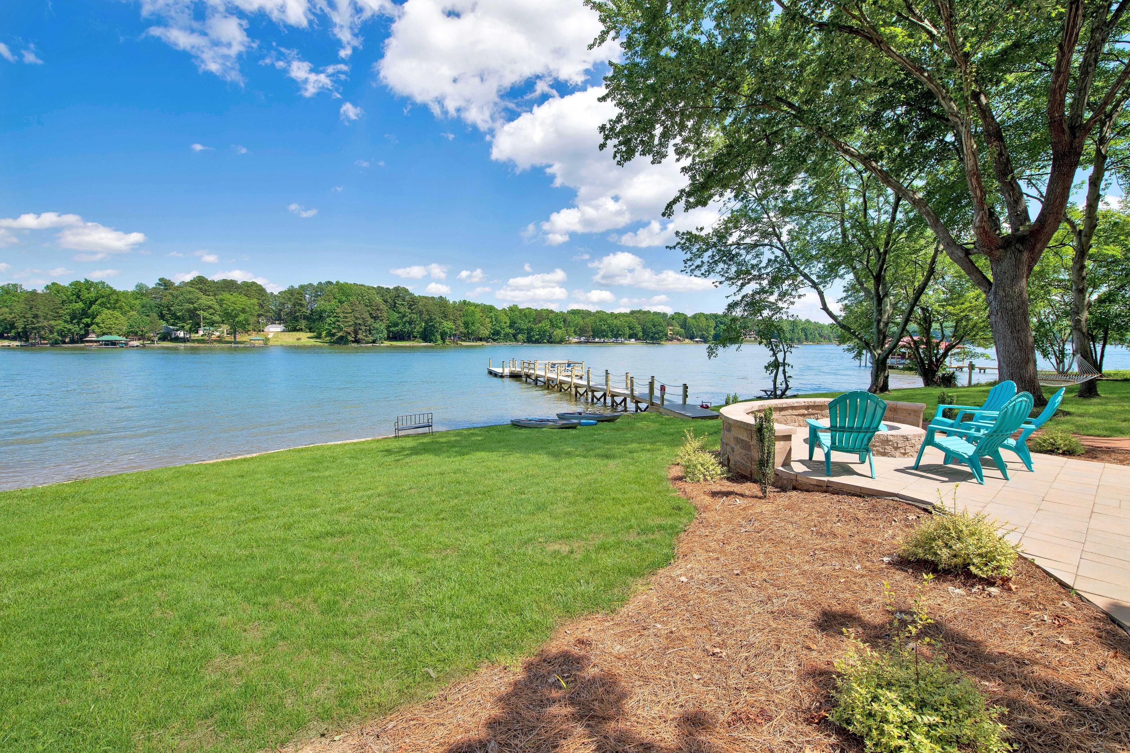 A lakeside patio with green chairs, a dock, and a grassy area.