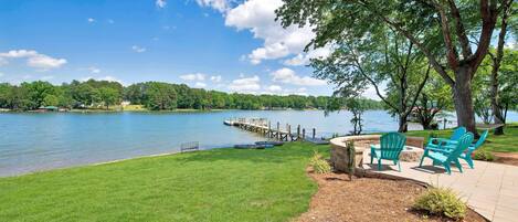 A lakeside patio with green chairs, a dock, and a grassy area.